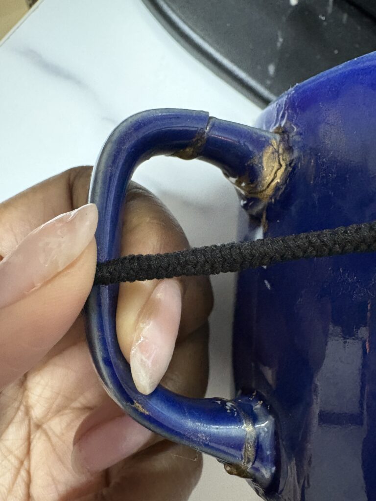 Close-up of a blue ceramic mug handle being carefully reattached using gold-accented adhesive during Kintsugi repair.