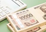 Stacks of Japanese 10,000 yen bills placed beside a white calculator on a pale green background