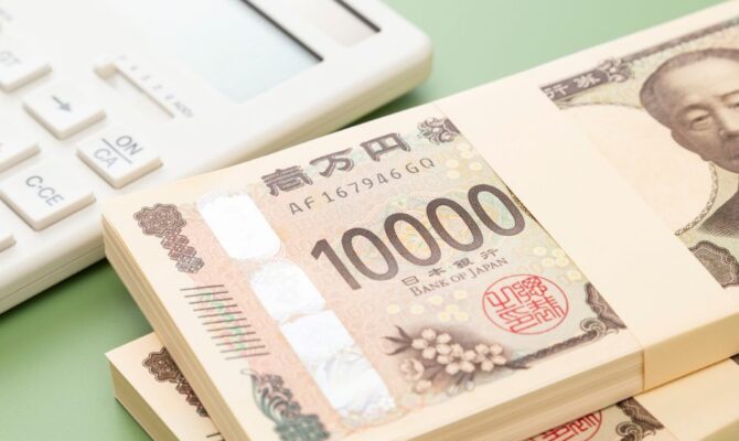 Stacks of Japanese 10,000 yen bills placed beside a white calculator on a pale green background