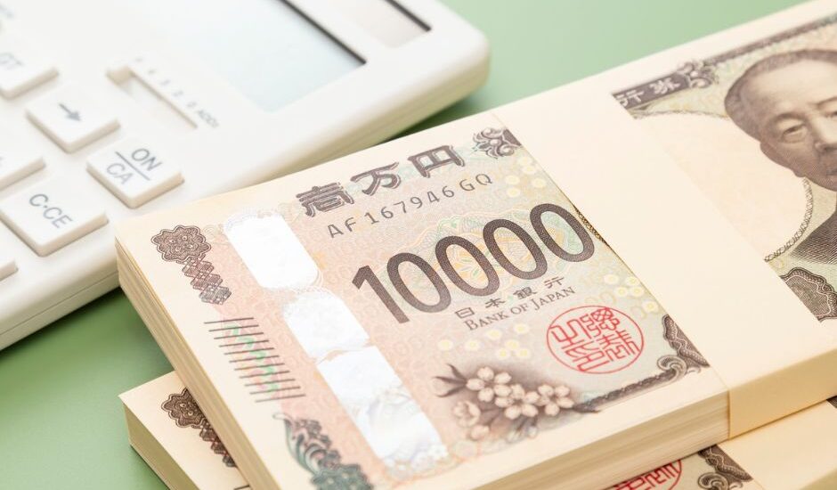 Stacks of Japanese 10,000 yen bills placed beside a white calculator on a pale green background