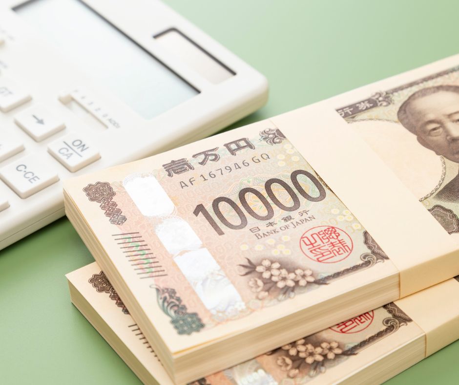 Stacks of Japanese 10,000 yen bills placed beside a white calculator on a pale green background