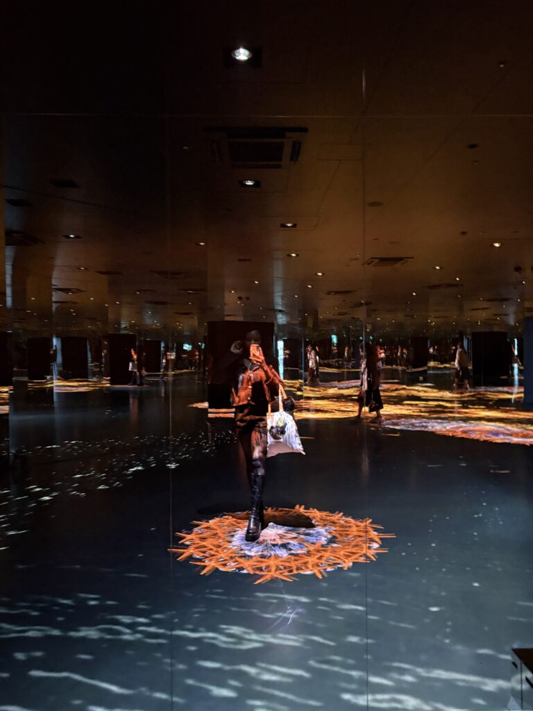 Visitor walking through immersive mirrored digital art room with glowing floor visuals at MIRACLE WORLD Osaka