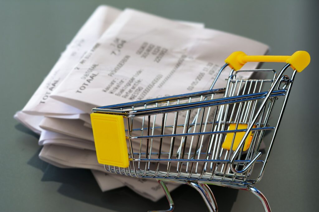 Small shopping cart placed in front of stacked grocery receipts, representing food expenses and supermarket budgeting.