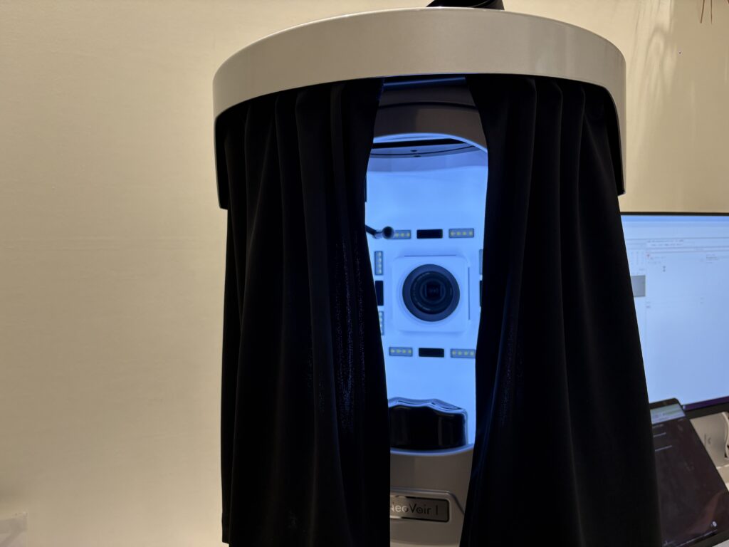 High-tech facial skin analysis machine with blue interior lighting and black curtains at a beauty clinic in Japan.