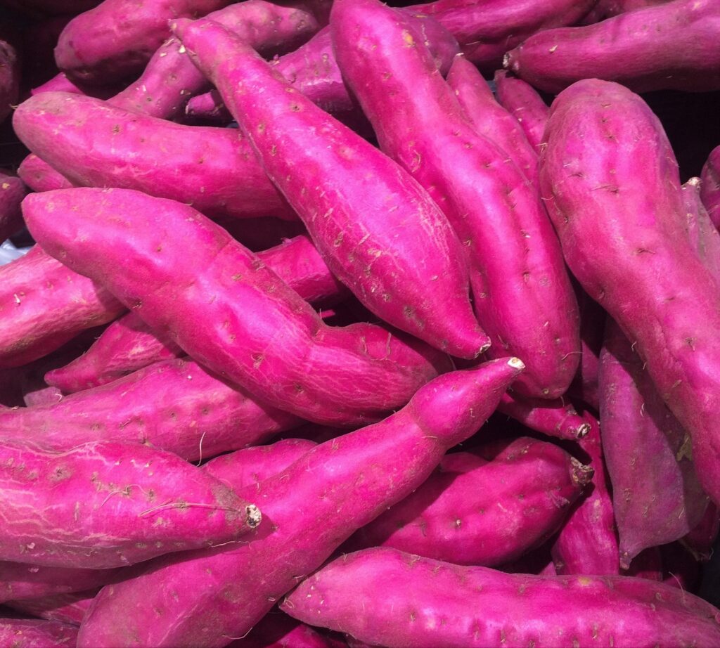 Pile of bright purple sweet potatoes stacked together in a produce section.