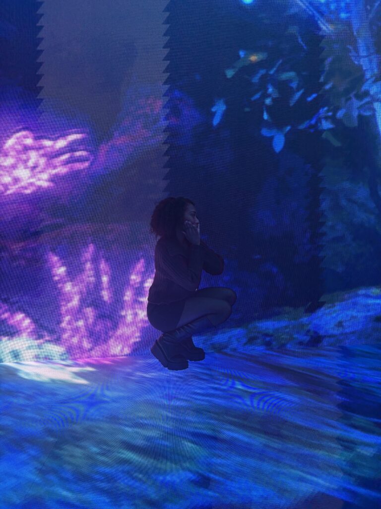 Woman sitting on ornate chair surrounded by large pink floral digital projections at MIRACLE WORLD