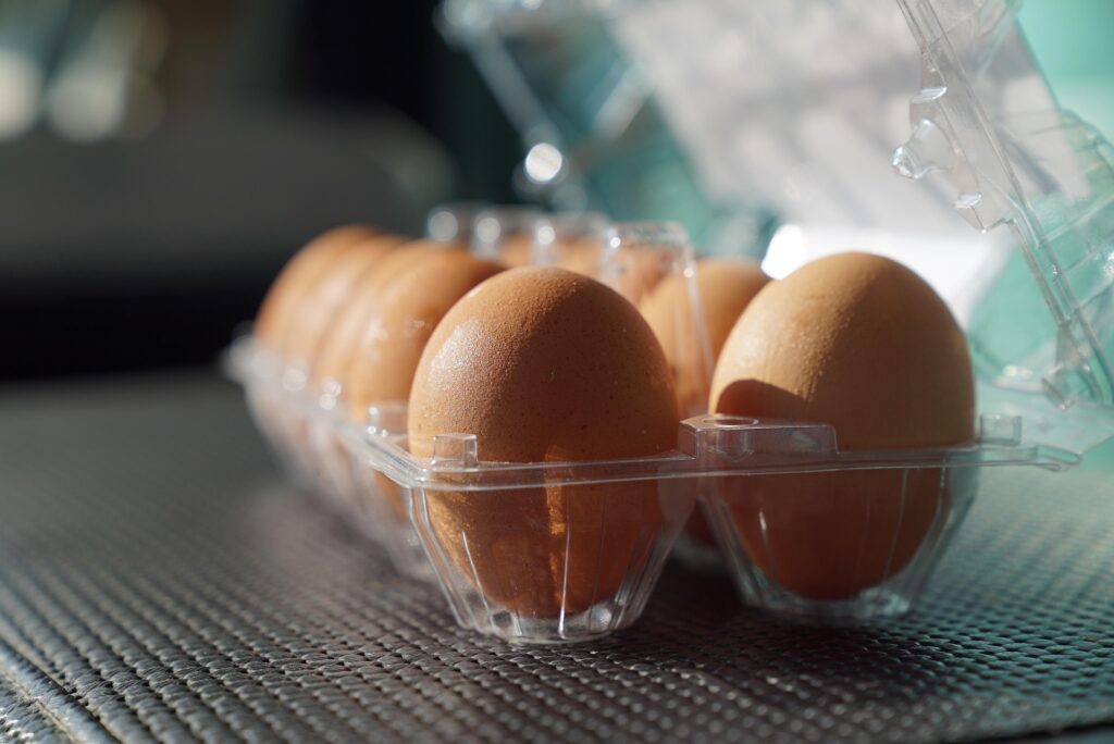 Brown eggs in a clear plastic carton with the lid open, placed on a textured surface.