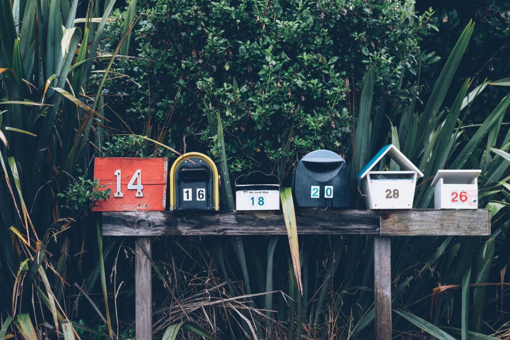Vintage red Japanese post box beside green bushes near a roadside path