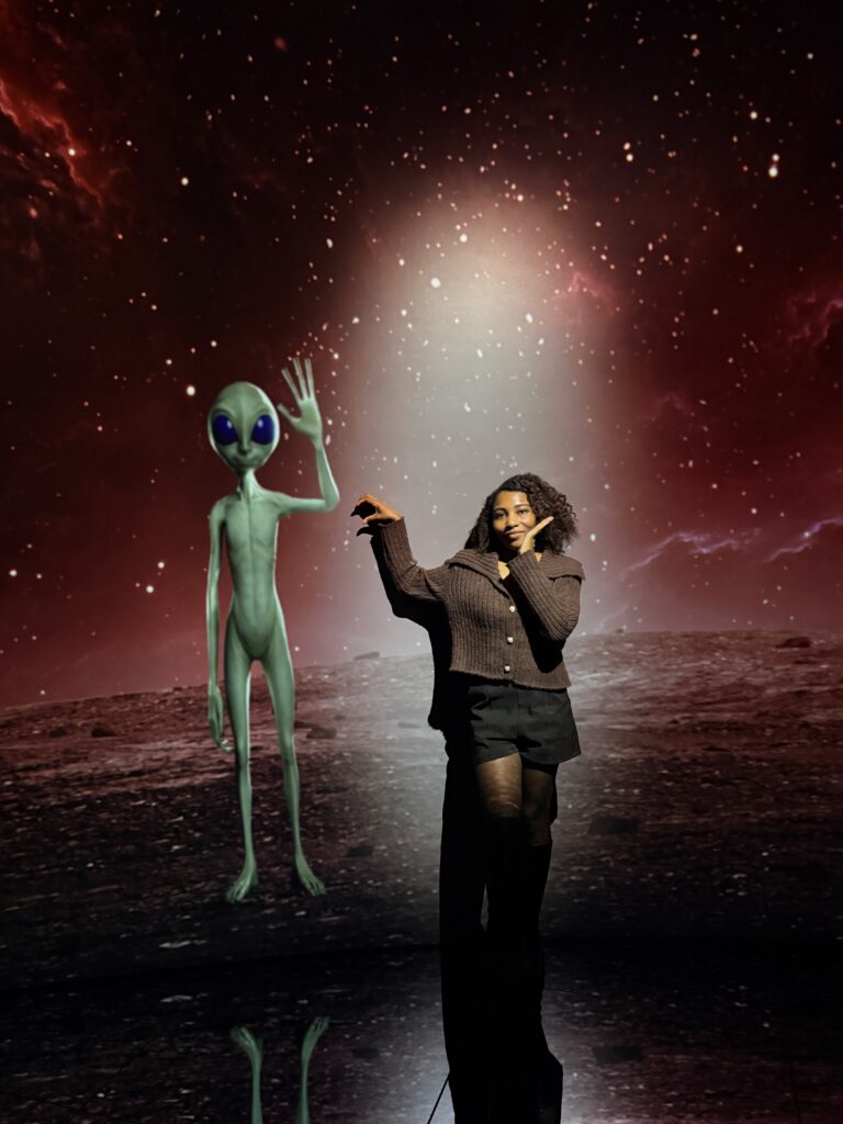 Visitor posing next to a green alien figure in a space-themed digital art room