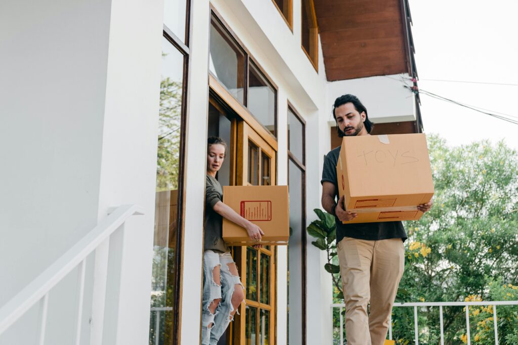 Couple carrying cardboard boxes out of a house during moving day.