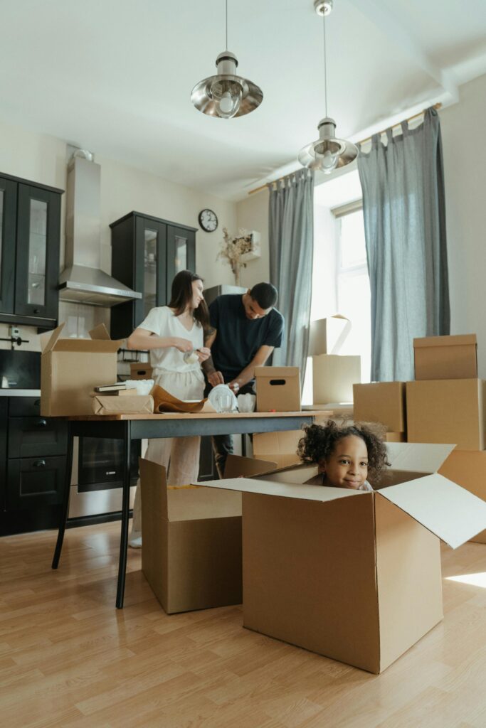 Woman smiling while holding a fragile moving box among stacked cardboard boxes.