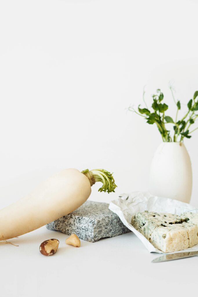 A large white daikon radish displayed on a table beside blue cheese and a small vase, representing Nerima’s agricultural heritage.