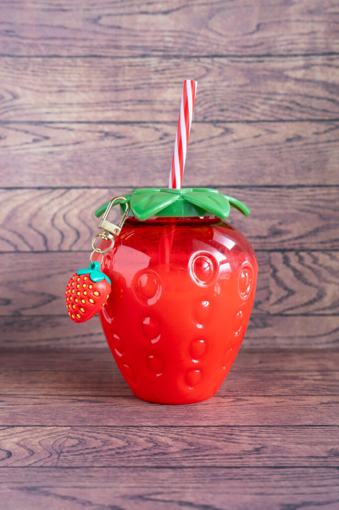 Strawberry milk drink served in a reusable strawberry-shaped bottle with a striped straw.