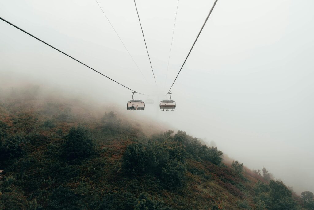 A ropeway gliding through thick fog above a forested mountainside in Tsukuba, creating a moody and misty view.