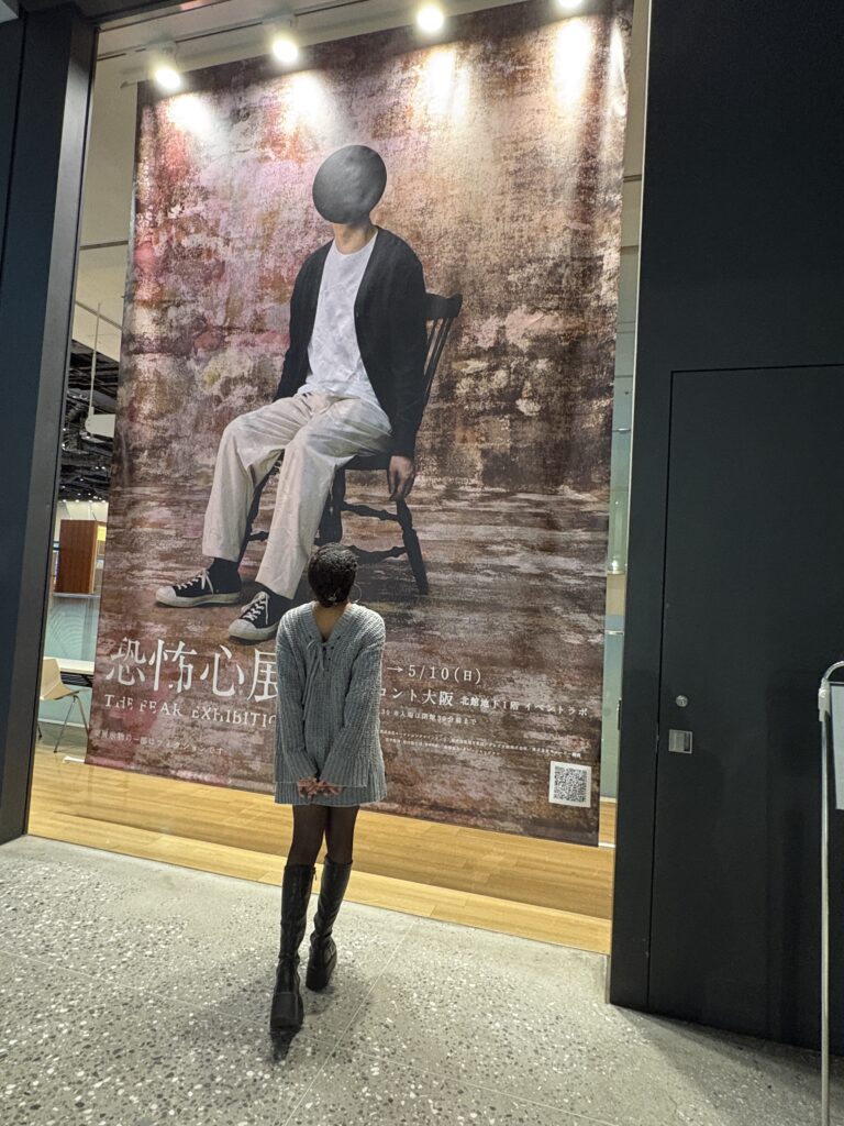 Woman standing in front of a large poster for The Freak Exhibition at an indoor venue in Osaka