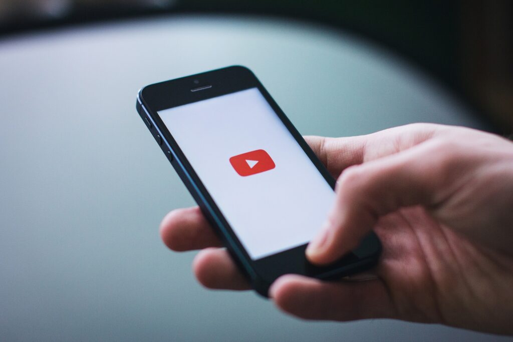 Hand holding a smartphone with the YouTube logo displayed on the screen