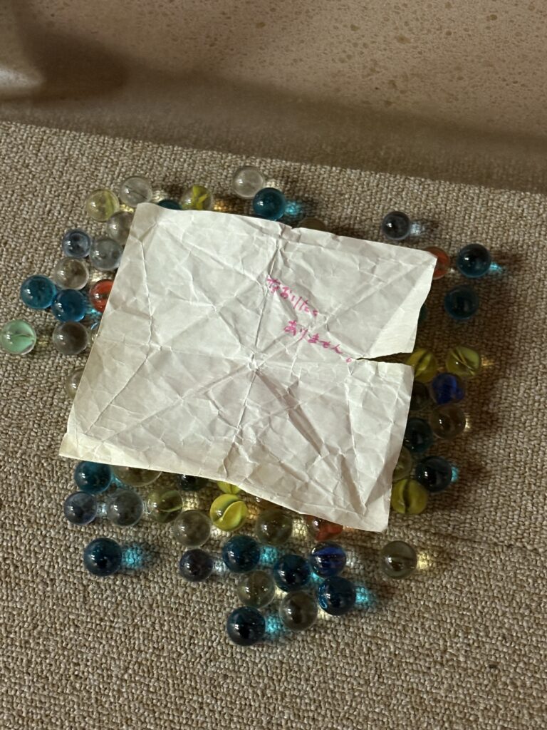 Crumpled handwritten note placed on the floor among scattered colorful glass marbles as part of an exhibit