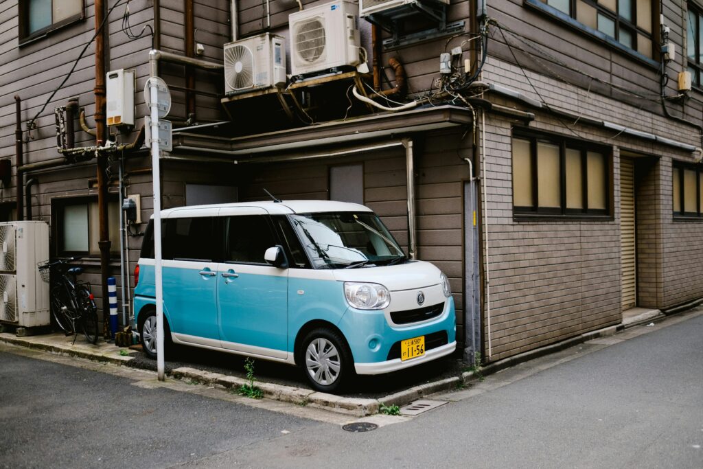 Outdoor air conditioner units mounted on the exterior wall of an older building beside a compact parked car.