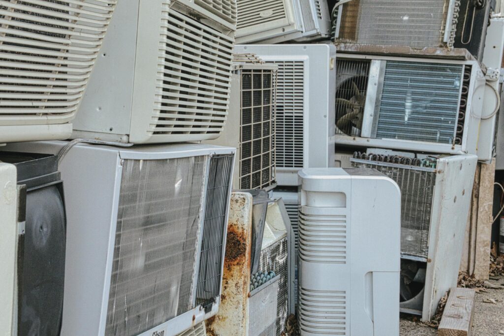Pile of old outdoor air conditioning units stacked closely together with visible wear and rust.