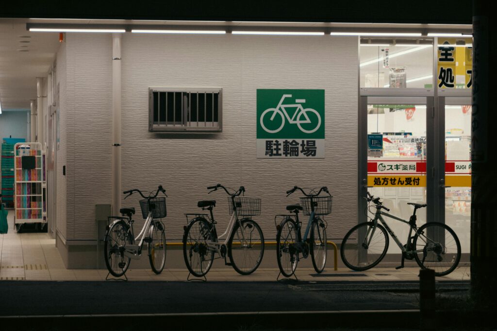 Several bicycles parked neatly outside a shop under a green bicycle parking sign at night in Japan