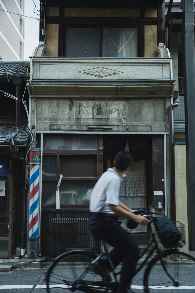 A man rides a bicycle past an old narrow building on a quiet street in Japan