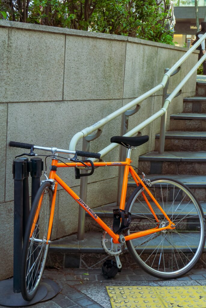 A bright orange sport bicycle locked beside a stairway in an urban area in Japan