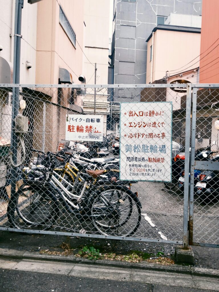 A fenced bicycle parking lot in Japan with signs warning against unauthorized bicycle and motorbike parking
