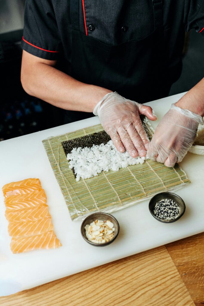 Bowl of freshly cooked sushi rice beside nori sheet and sliced cucumber ready for sushi preparation