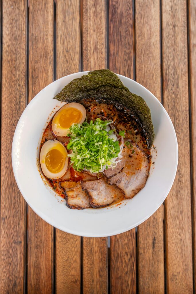 Bowl of ramen topped with slices of pork, soft-boiled eggs, green onions, and a sheet of nori