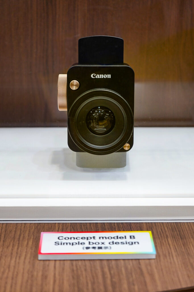 Canon concept camera model B on display at CP+ 2026, showing a simple box-shaped body with gold accent details and a large front lens.