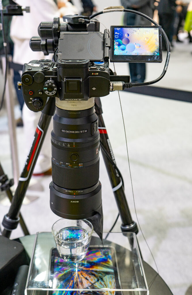 Sony macro photography demo setup with a mirrorless camera mounted on a tripod, a large macro lens, and a close-up subject placed below for testing.