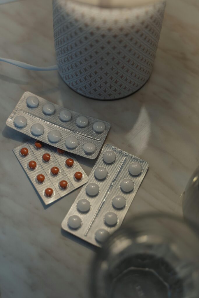 Blister packs of allergy tablets and capsules placed on a marble surface beside a softly lit diffuser and a glass of water.