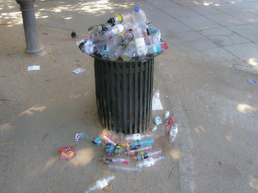 Overflowing public trash bin filled with plastic bottles and recyclable waste outdoors.