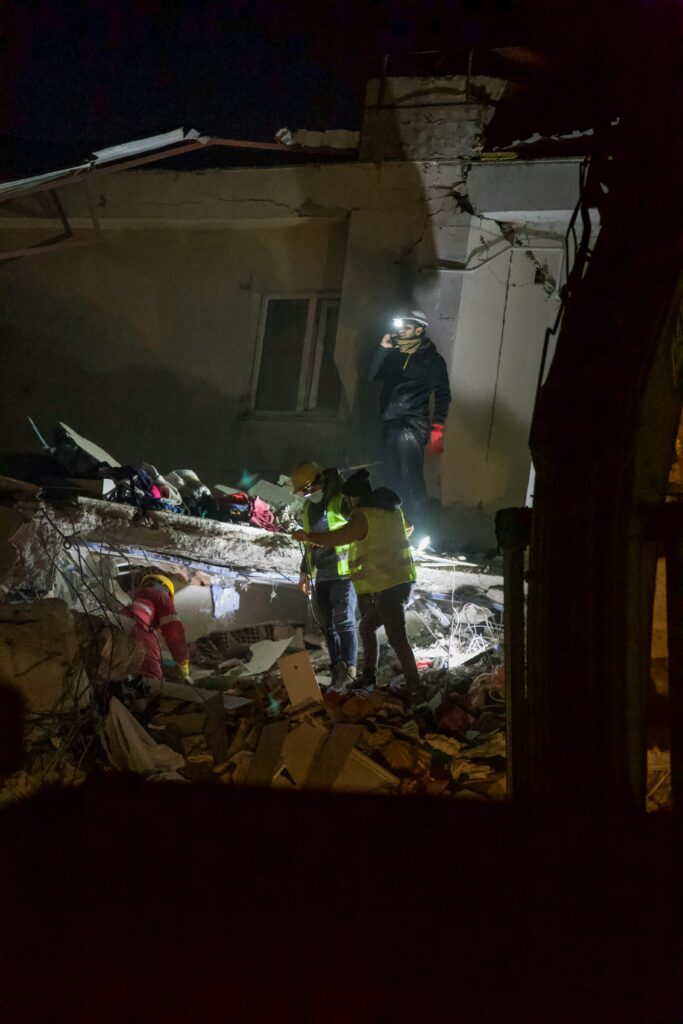 Rescue workers using lights to search damaged buildings at night after an earthquake.