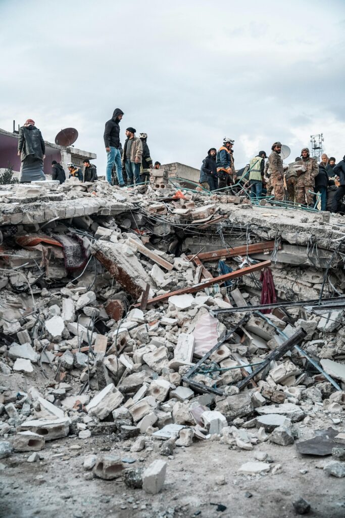 People standing among collapsed buildings and earthquake rubble after a disaster.