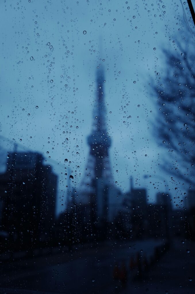 View of Tokyo Tower blurred behind raindrops on a window, capturing the gloomy atmosphere of a rainy day in Tokyo.