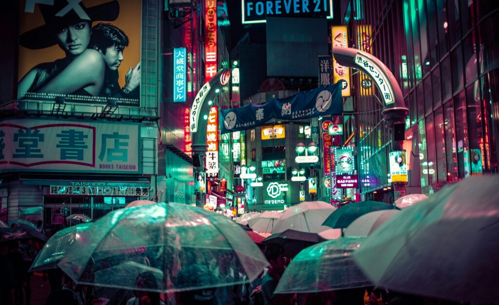Neon-lit streets in Shibuya filled with transparent umbrellas during a rainy night in Tokyo, capturing the busy atmosphere of Japan’s rainy season.
