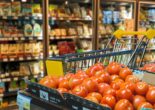 Shopping cart beside fresh tomatoes and refrigerated food shelves inside a modern supermarket grocery store.