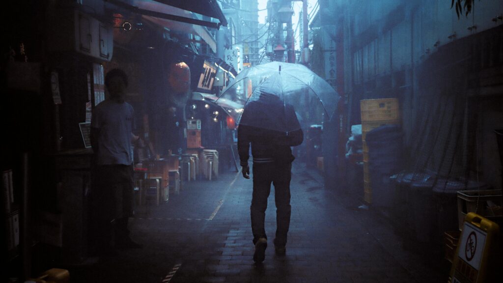 A person walking through a dark Tokyo alley under an umbrella during heavy rain and typhoon weather.