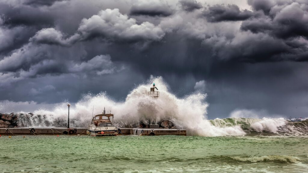 Huge waves crashing against a harbor during stormy weather as dark clouds gather overhead.