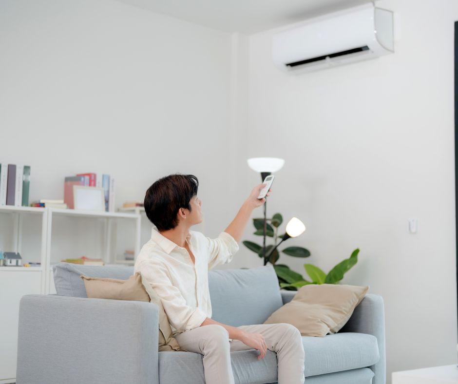 Person adjusting a wall-mounted air conditioner in a Japanese apartment.