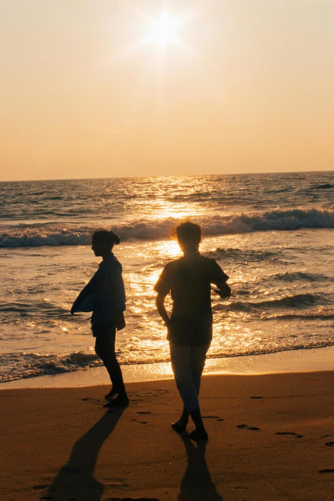 Golden sunset reflects across gentle ocean waves with silhouetted hills lining the horizon.