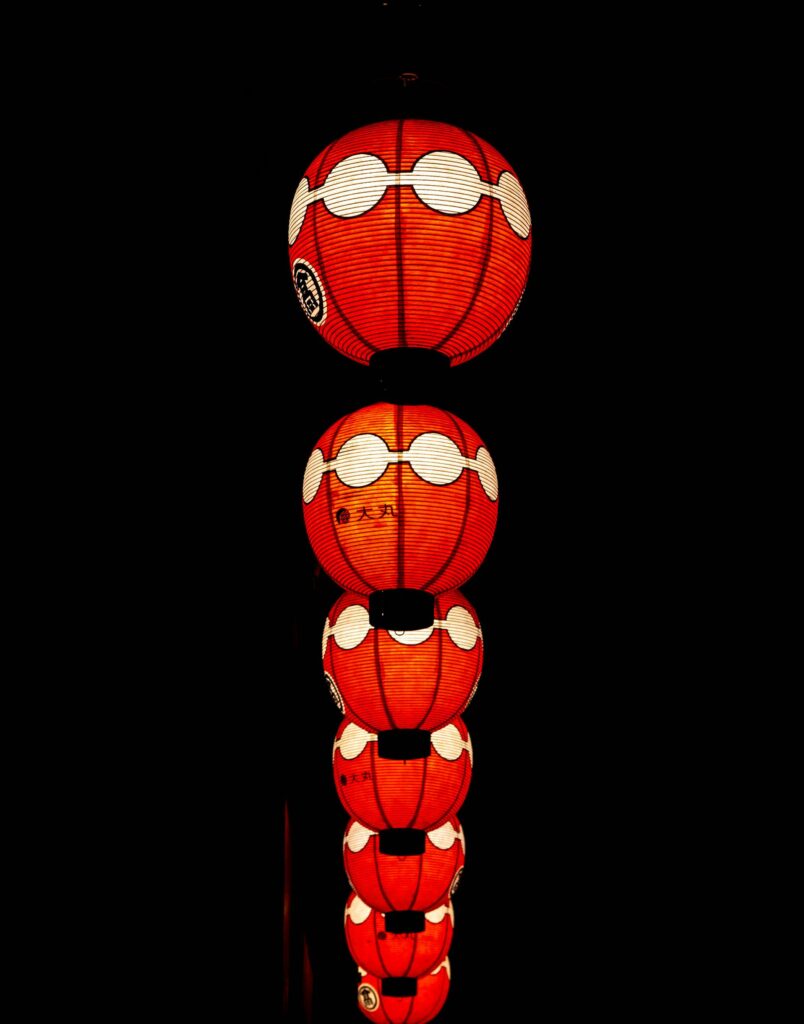 A row of glowing red paper lanterns lights up the night during a traditional Japanese neighborhood festival.
