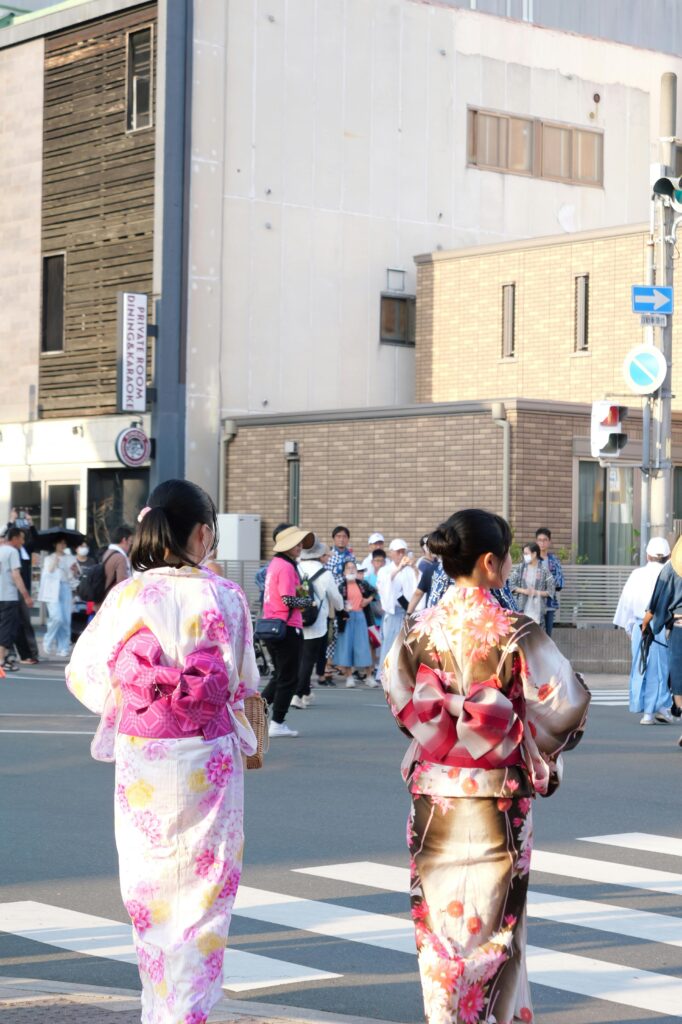 Two women wearing colorful yukata walk through the streets toward a local Japanese summer festival.
