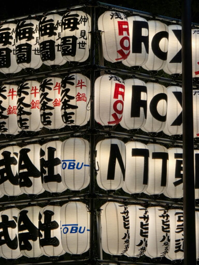 Rows of sponsored paper lanterns illuminate the festival grounds during a traditional Japanese matsuri at night.