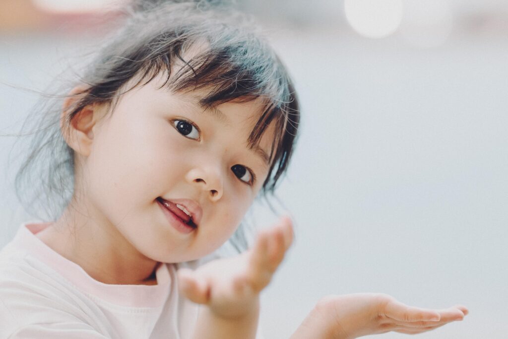 Close-up of a young child smiling with hands raised, representing curiosity, learning, and enjoying summer vacation.