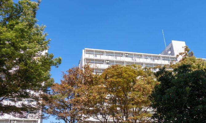 Apartment building in Japan surrounded by green and autumn-colored trees under a clear blue sky.