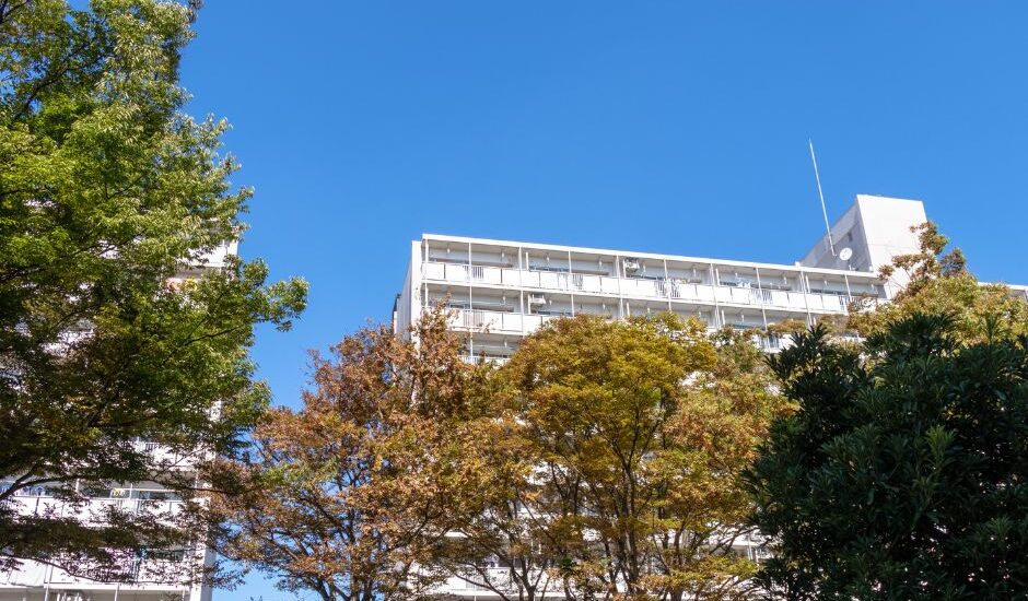 Apartment building in Japan surrounded by green and autumn-colored trees under a clear blue sky.