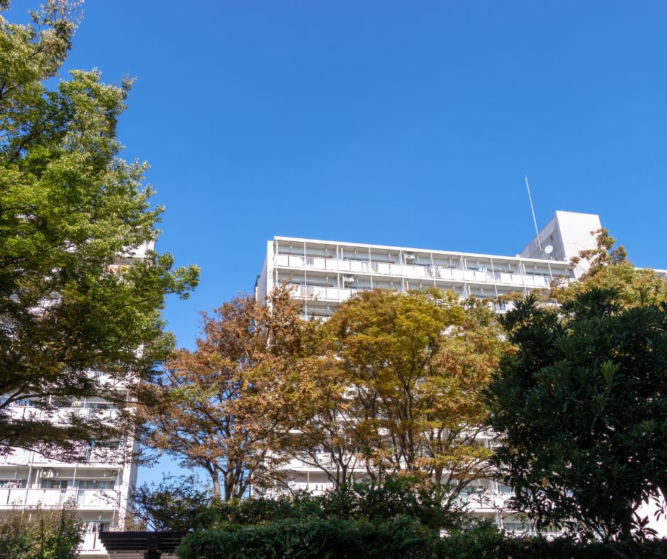 Apartment building in Japan surrounded by green and autumn-colored trees under a clear blue sky.