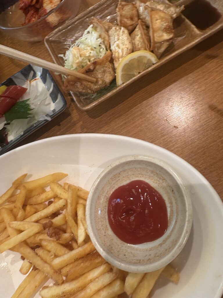 A table filled with izakaya dishes, including French fries and fried chicken, during a break from the mystery adventure.
